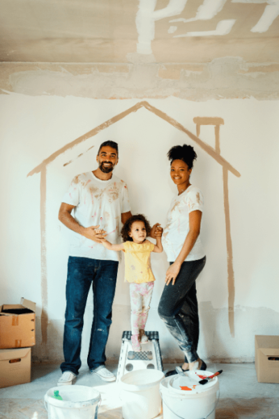 photo d'une famille avec monsieur et madame enceinte, et une petite fille au milieu. ils ont dessiné une maison sur le mur